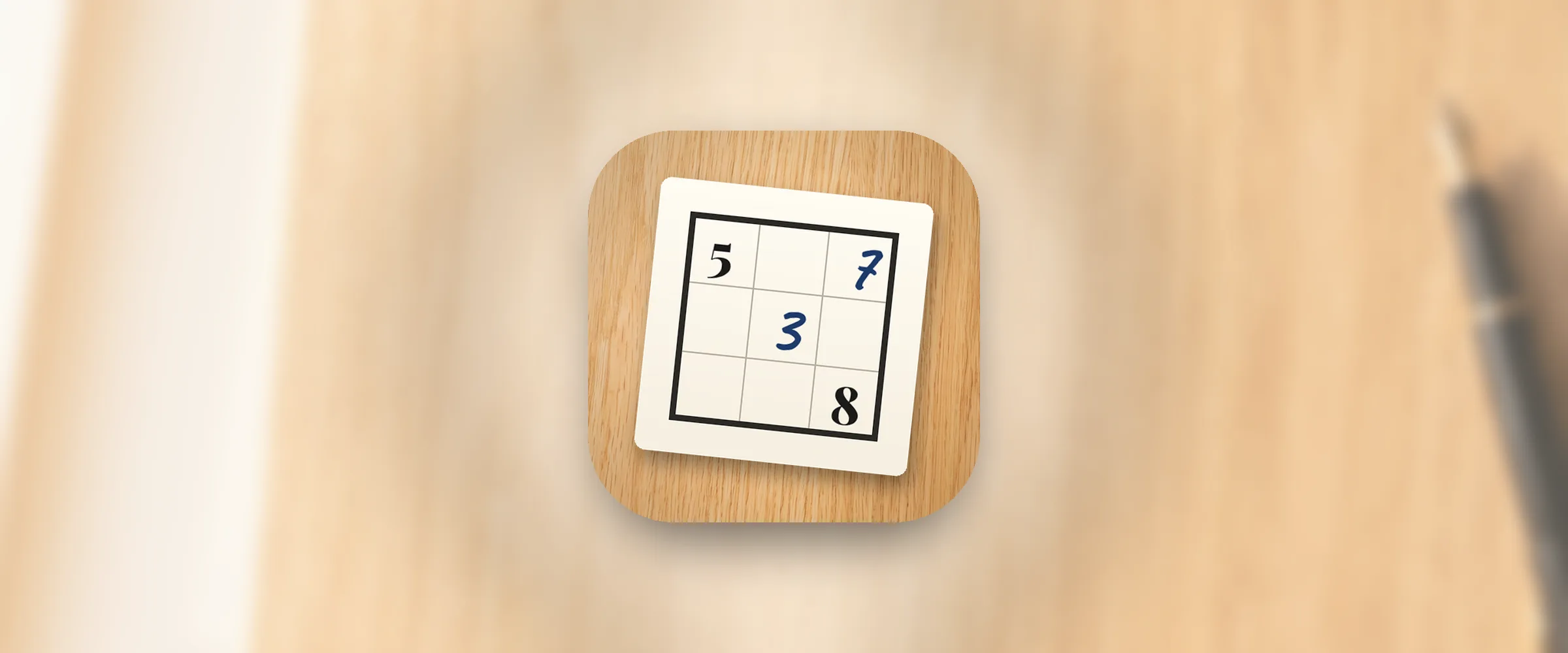The Inkwell Sudoku icon, a cream paper card with a small three-by-three sudoku box, printed numbers and blue handwritten ink, on a light oak desk